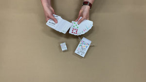 Video of a woman taking the poker-size travel domino playing cards out of the box, and running them through her hands to show how many cards there are (92+). Then she picks up the domino-sized cards and does the same. Both cards and both boxes are on the same table next to each to compare sizes.