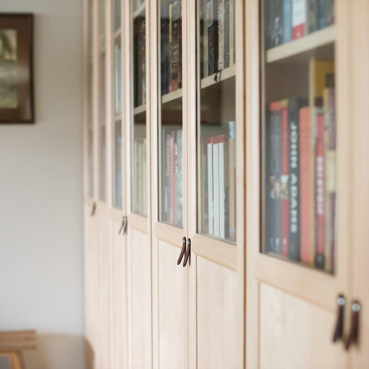 Still life image of the dark brown leather small handle on a birch wood BILLY bookcase from IKEA with the glass doors on top and books behind it. Taken from an angle looking down a line of bookcases.