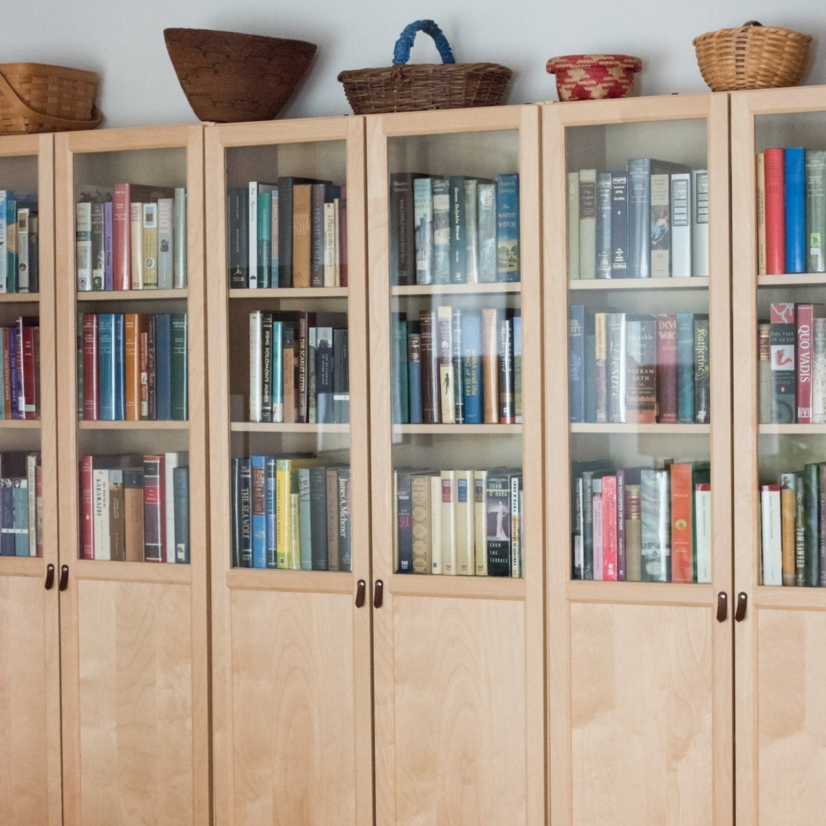 Still life image of the dark brown leather small handle on a birch wood BILLY bookcase from IKEA with the glass doors on top and books behind it. From across the room.