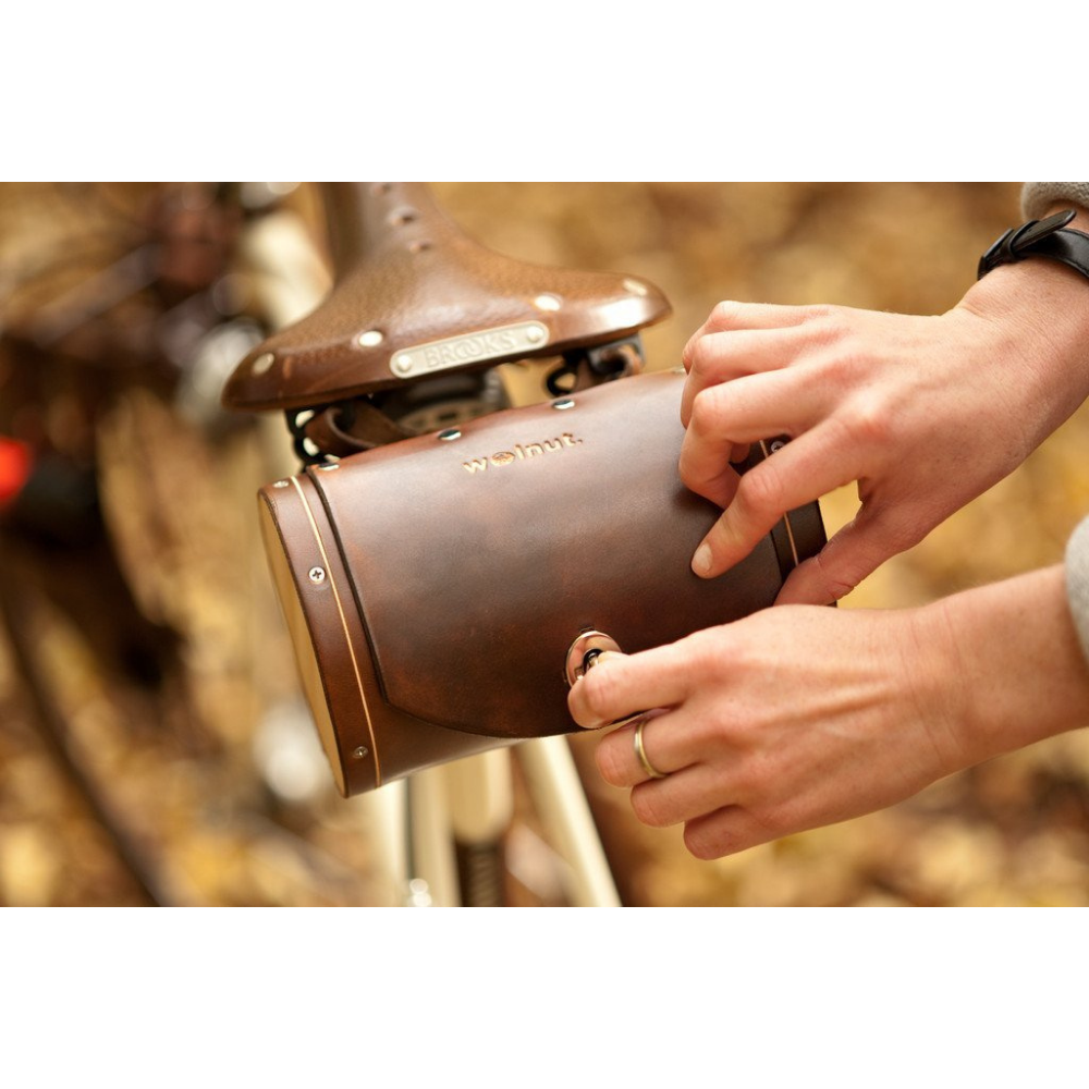 Hand opening dark brown leather barrel bag attached to saddle 