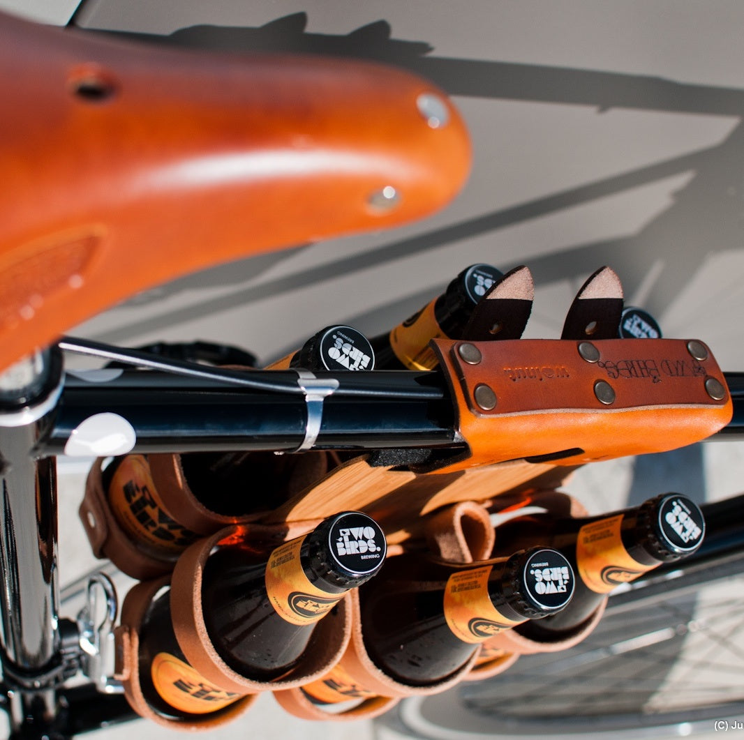 Honey leather and bamboo six-pack held on the top tube of a black bicycle with a 6-pack beer carrier, the 6-pack frame cinch on a custom branded bike for an Australian brewery