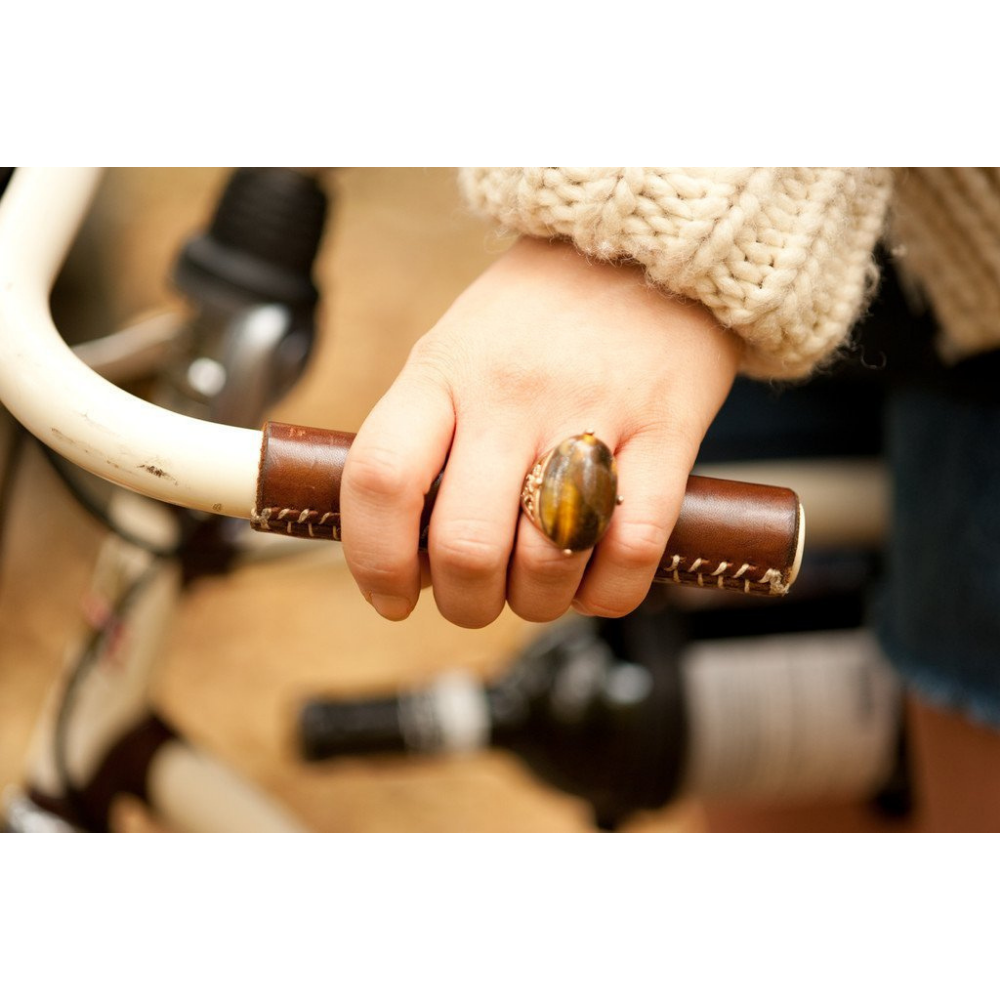 Woman wearing a chunky tiger&#39;s eye gemstone ring that matches the dark brown leather city grip on her bicycle handlebar