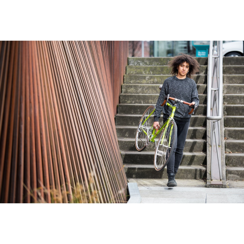 Black cyclist walking down urban stairs holding a lime green bicycle with honey leather frame handle and handlebar wraps.