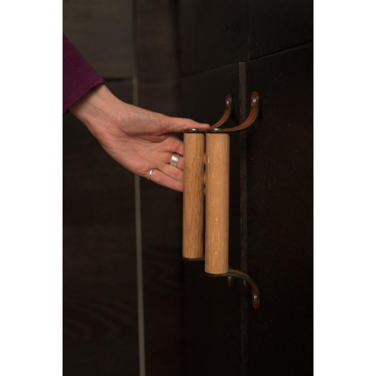 Taken at a 45 degree angle showing the projection, two leather and wood Sellwood handles with honey leather on a black-brown cabinet surface. 