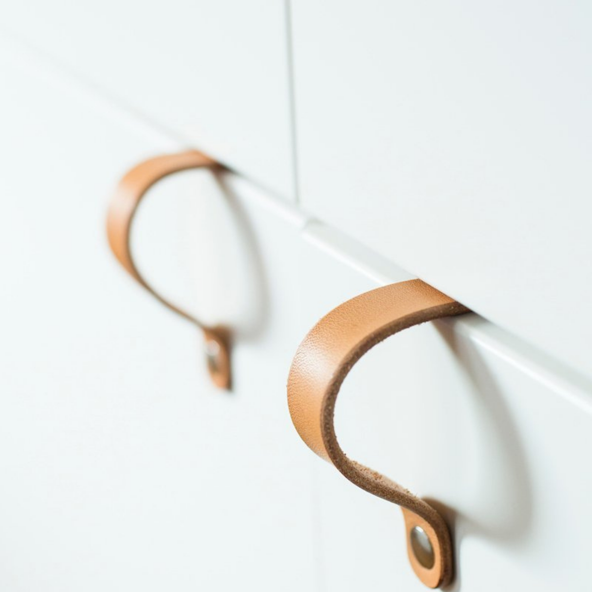 Woman is pulling open a bottom cabinet door under sink with a natural leather Lovejoy handle. On top of the cabinet is the two tiny wood screws that attach the handle to the IKEA cabinet door.