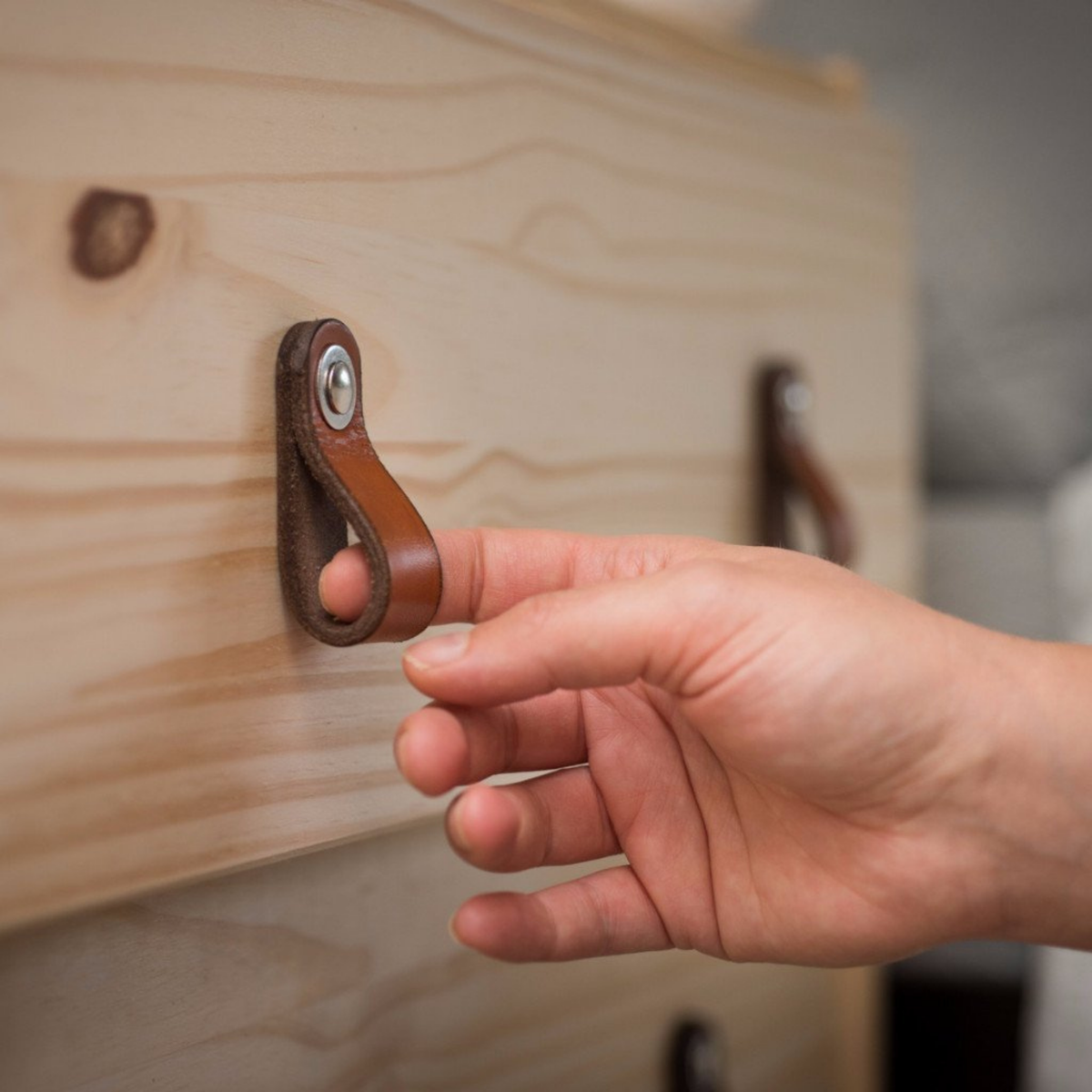 Woman&#39;s hand reaching out to a small honey-colored leather handle and pulling out a knotty pine wood drawer