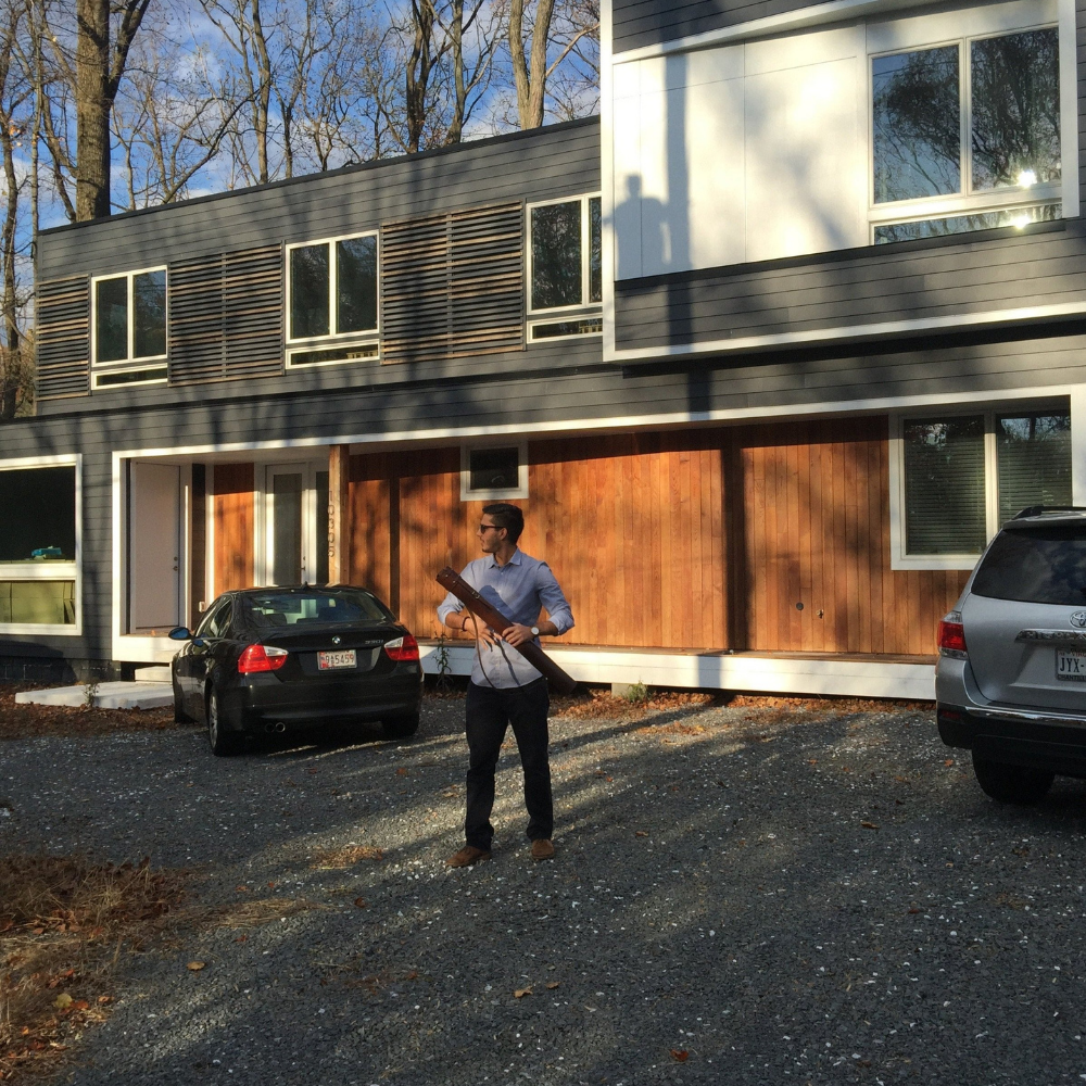 Man holding dark brown architect tube in front of house