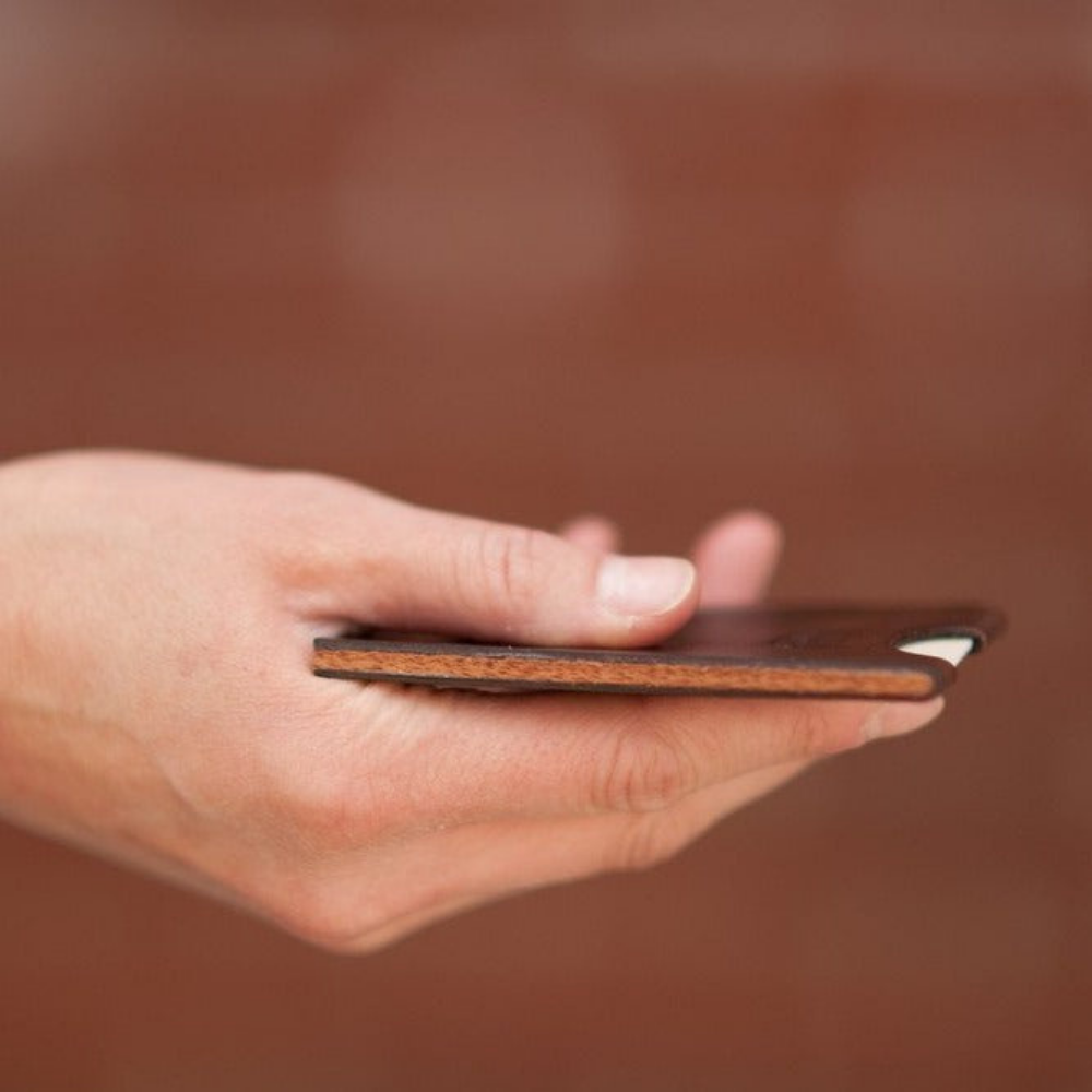 Hand holding minimalist leather card wallet to showcase walnut wood center