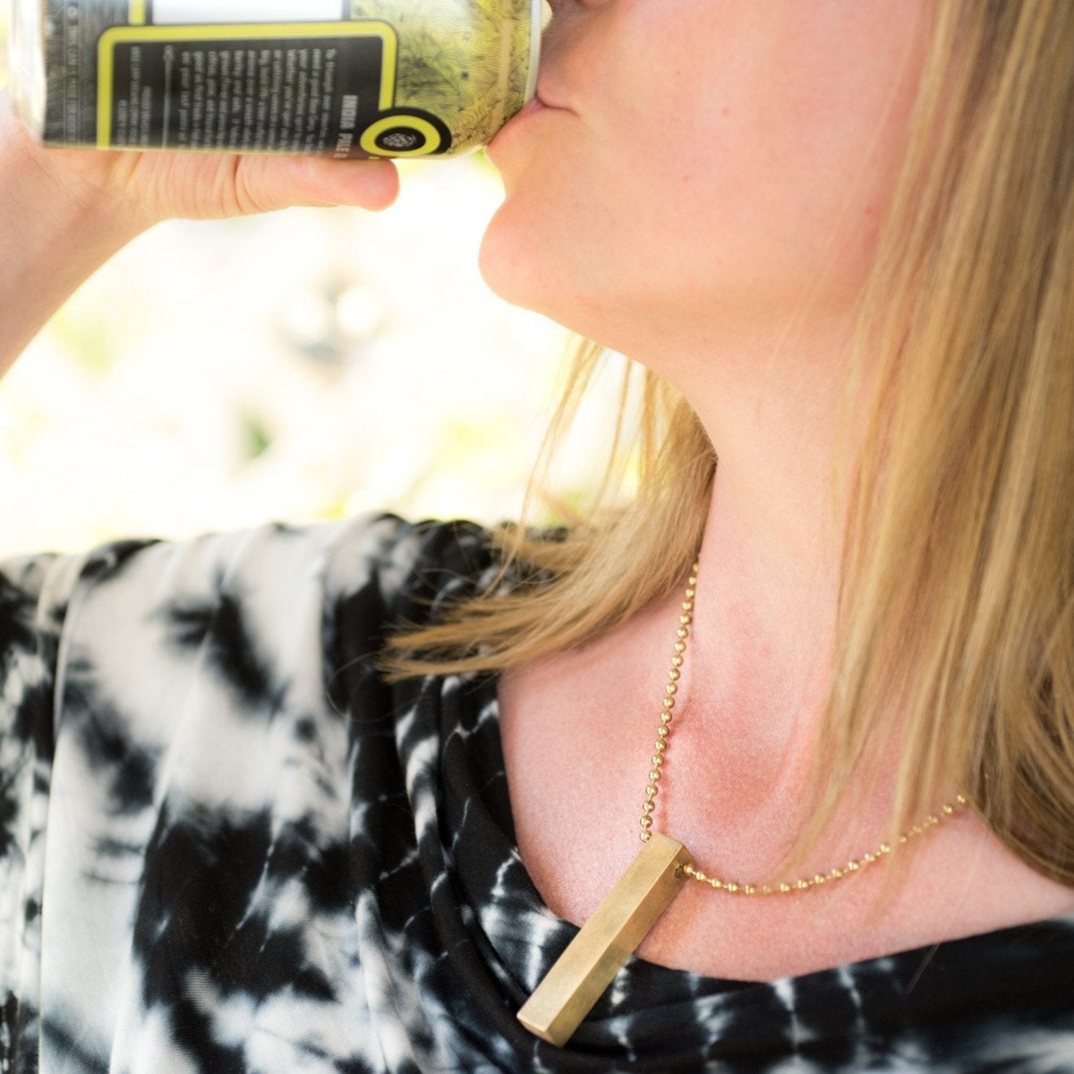 Close-up of a woman&#39;s neck and collarbone, wearing the square brass travel dice as a necklace using a longer section of brass beaded chain. 